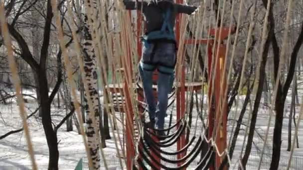 Joven escaladora camina por puente de cuerda colgante en el curso de cuerdas altas en el parque extremo. Concepto de escalada — Vídeos de Stock