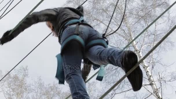 Νεαρή γυναίκα ορειβάτης βόλτες από γέφυρα σχοινί κρεμαστό κόσμημα στην υψηλή σχοινιά σε ακραίες πάρκο. Έννοια αναρρίχησης βράχου — Αρχείο Βίντεο