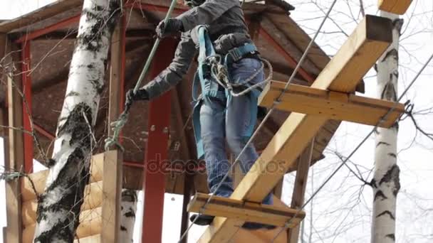 Молода жінка альпіністка прогулюється підвісним мостом на високих мотузках в екстремальному парку. концепція скелелазіння . — стокове відео