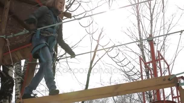 Giovane arrampicatrice passeggia a ciondolo ponte di log su un percorso di corde alte in un parco estremo — Video Stock