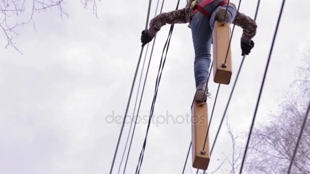 Молодой альпинист ходит по бревенчатому мосту на высоких канатах в экстремальном парке — стоковое видео