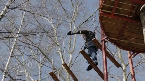 Joven escaladora camina por puente de tronco colgante en curso de cuerdas altas en parque extremo — Vídeo de stock