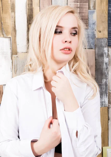Retrato de chica rubia atractiva de pie sobre fondo de pared de madera. Tiene ojos azules y está vestida con una camisa de hombre. — Foto de Stock