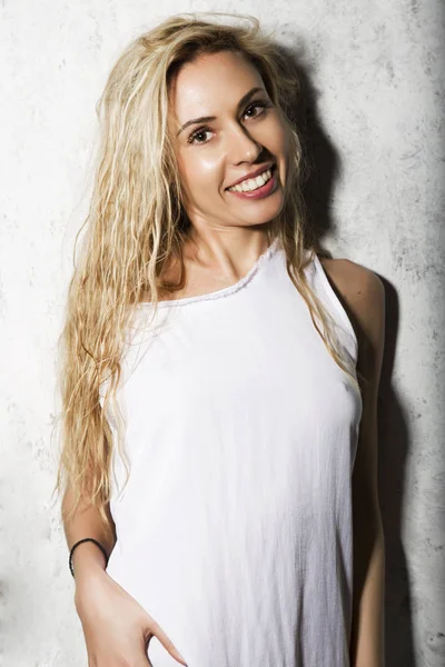 Moteportrett av blond modell som poserer nær grå vegg, jente i hvite skjorter som smiler – stockfoto