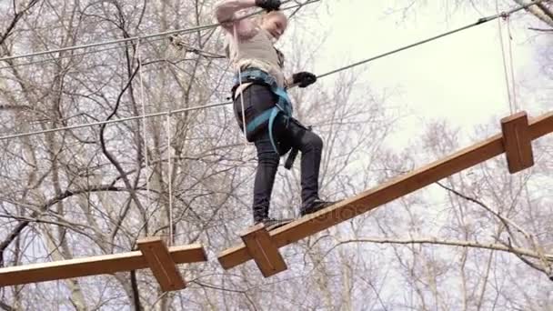 Mladý teenager horolezec chodí přívěsek dřevěný most na vysokých lanových překážek v extrémních parku — Stock video