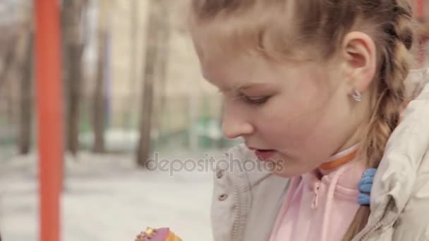 Tiener meisje eten van een donut in een outdoor park — Stockvideo