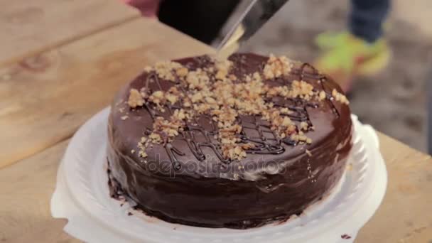 Persoon snijden de chocolade taart met een mes op een houten tafel — Stockvideo