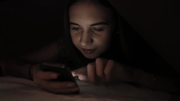 Chica joven que se esconde bajo edredón y el uso de dispositivo tableta PC en la oscuridad. Adolescente jugando en una tableta digital por la noche . — Vídeo de stock