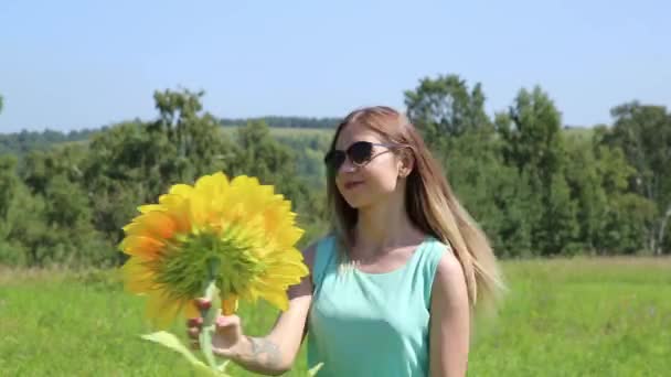 Молодая девушка крутится на зеленой траве, держа подсолнух — стоковое видео