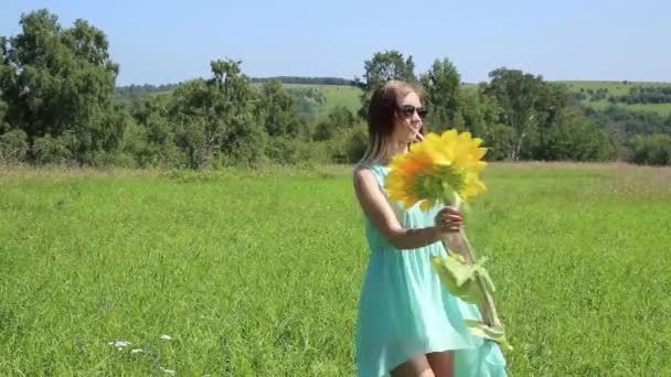Jong meisje spinnen op een groen gras, houden van de zonnebloem — Stockvideo