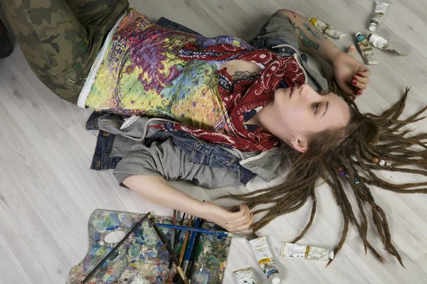 有吸引力的年轻女艺人与长发绺躺在地板上，持有画笔，还有附近的颜料管 — 图库照片