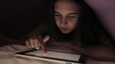 genç kız karanlıkta yorgan ve kullanım pc tablet cihaz altında saklanıyor. Dijital bir tablete geceleri oynayan genç.