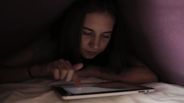 Mladá dívka schovává pod peřinu a použití zařízení tablet pc ve tmě. Teenager hrál na digitálním tabletu v noci. — Stock video