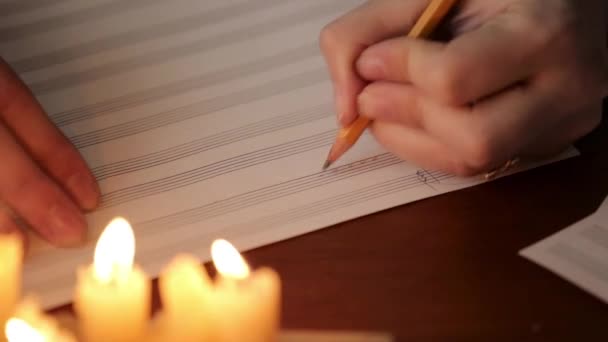 Estudante escrevendo uma música: músico compondo com um lápis em um livro de música com luz de velas. mão close-up do músico — Vídeo de Stock