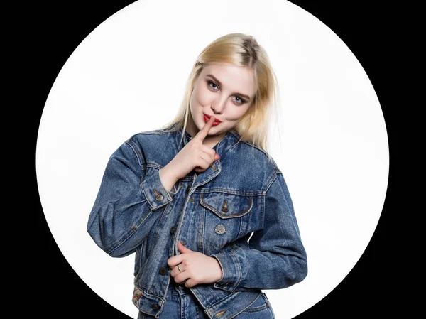 Junge blonde Frau in Jeansjacke und Jeans zeigt Zeigefinger zu den Lippen auf weißem Hintergrund — Stockfoto