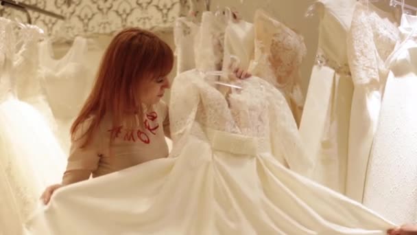 Jolie jeune femme choisissant une robe de mariée. assistant de magasin aide pour une fille dans le magasin de mariage . — Video