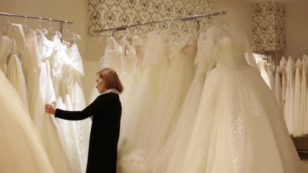 Молодая красивая женщина выбирает белое платье в свадебном магазине. Концепция — стоковое видео
