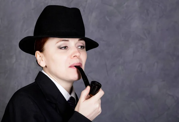 Hermosa mujer en estilo varonil con pipa de fumar sobre fondo gris, chica en traje y corbata de hombre, camisa blanca y sombrero — Foto de Stock