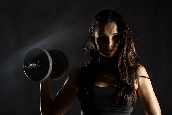 Σέξι κοπέλα γυμναστικής με αλτήρες σε σκούρο φόντο. Αθλητής που κάνει ασκήσεις στο γυμναστήριο — Φωτογραφία Αρχείου