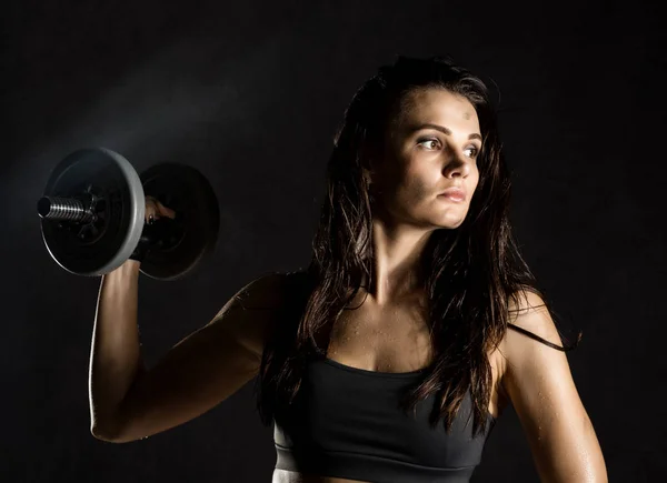 Koyu arkaplanda halterleri olan seksi bir kız. Sporcu spor salonunda egzersiz yapıyor. — Stok fotoğraf