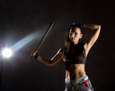 beysbol sopası üzerinde koyu arka planda bir projektör demeti ile seksi atletik kadın