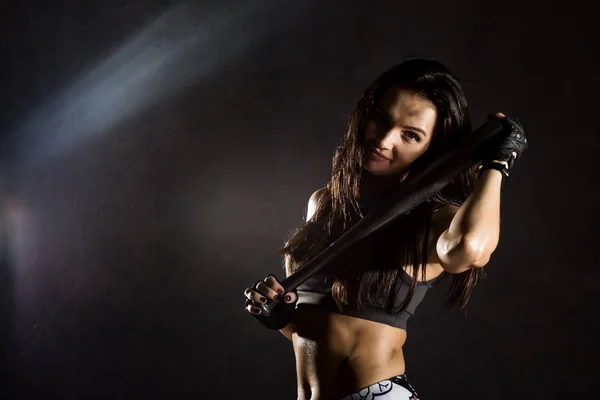 Sexy athletic woman with baseball bat on dark background in the beam of a searchlight — Stock Photo, Image