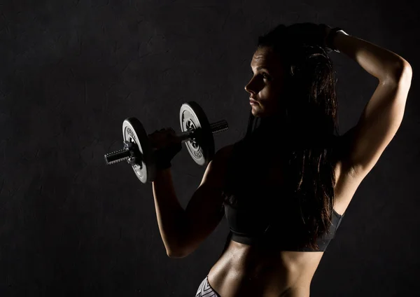 Фитнес сексуальная девушка с гантелями на темном фоне. Спортсмен делает упражнения в спортзале — стоковое фото