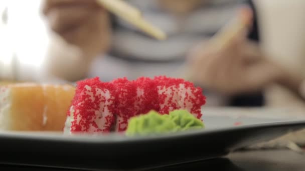 Две счастливые женщины едят суши в ресторане японской кухни, используют палочки для еды. рулоны крупным планом на тарелке — стоковое видео