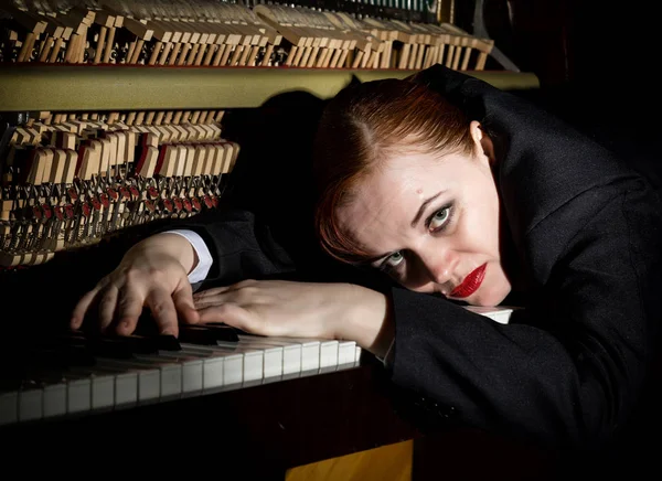 Женщина-музыкант в костюме мужчины лежит на фортепианной клавиатуре — стоковое фото