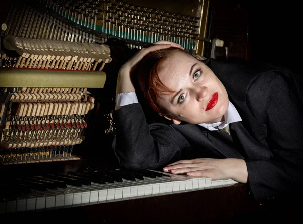 Женщина-музыкант в костюме мужчины лежит на фортепианной клавиатуре — стоковое фото