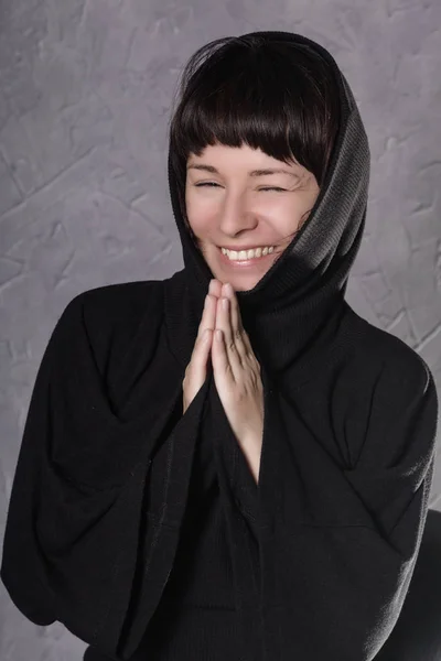 Mujer rezando en vestido negro con capucha sobre un fondo gris — Foto de Stock