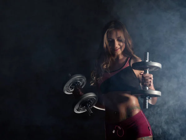 Gimnasio joven en el entrenamiento con pesas, deportivo musculoso morena femenina en el humo — Foto de Stock