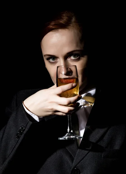 Mulher estranha em um terno de homem bebe champanhe em um fundo escuro — Fotografia de Stock
