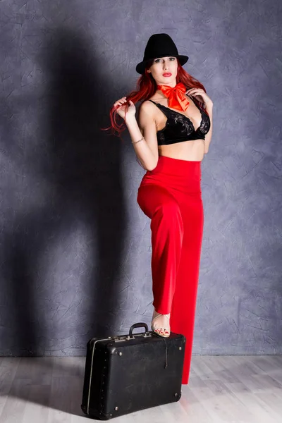 Donna in pantaloni rossi e cappello nero con grandi tette tenere valigia retrò — Foto Stock