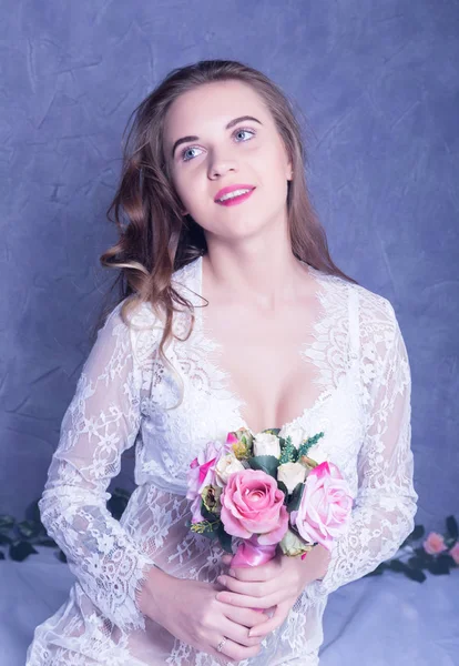 Hermosa novia en un peignoir blanco con un ramo de flores — Foto de Stock