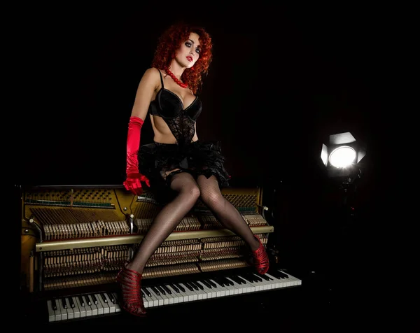 Ragazza sexy sembra una bambola con la rossa riccia siede su un pianoforte, su uno sfondo grigio. Stile di moda — Foto Stock