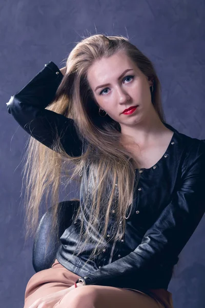 Hermosa mujer joven en una chaqueta de cuero posando sobre un fondo gris —  Fotos de Stock