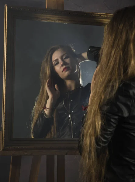 Piękna młoda kobieta w skórzanej kurtce wygląda w lustrze jako jej portret — Zdjęcie stockowe