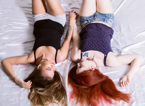 Zwei Freundinnen, die sich auf einem Bett im hellen Schlafzimmer umarmen und küssen. lesbisches Paar mit Teddybär — Stockfoto