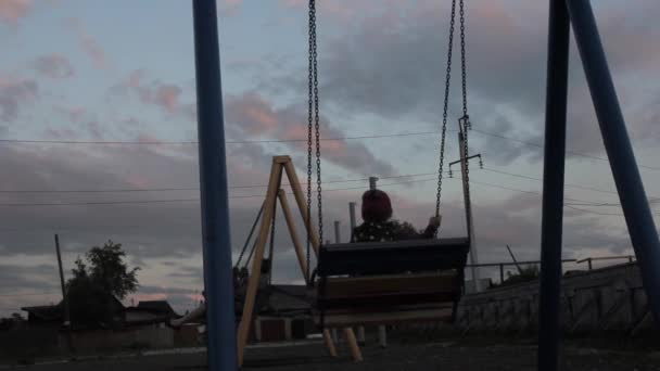 Niño triste balanceándose sobre un columpio sobre un fondo de cielo oscuro. maltrato infantil, infancia dolorosa — Vídeo de stock