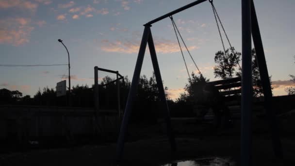 Niño triste balanceándose sobre un columpio sobre un fondo de cielo oscuro. maltrato infantil, infancia dolorosa — Vídeos de Stock