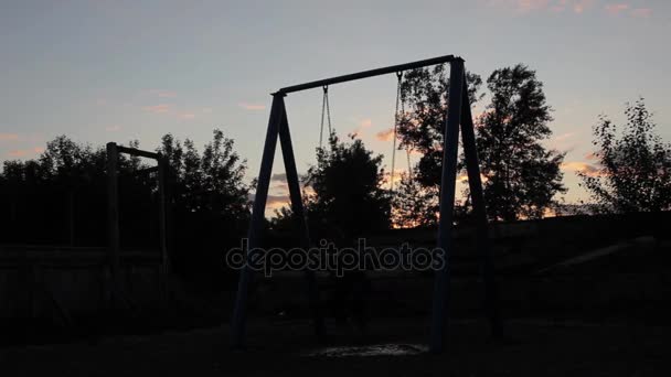 Niño triste balanceándose sobre un columpio sobre un fondo de cielo oscuro. maltrato infantil, infancia dolorosa — Vídeos de Stock