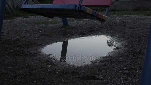 Opuštěné dětské hřiště, nevinnost smutné dítě houpat na houpačce. odraz v kalužích. — Stock video