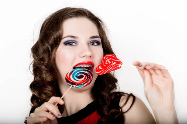 Chica sonriente con frenillos sosteniendo caramelos del corazón posando sobre un fondo blanco — Foto de Stock