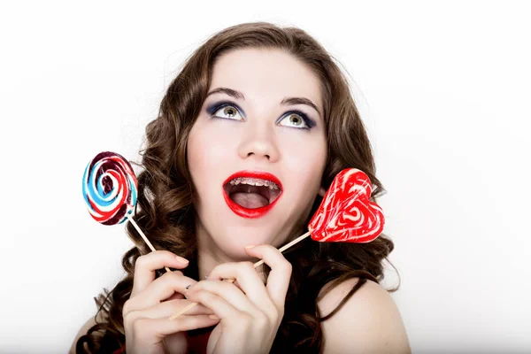 Chica sonriente con frenillos sosteniendo caramelos del corazón posando sobre un fondo blanco — Foto de Stock