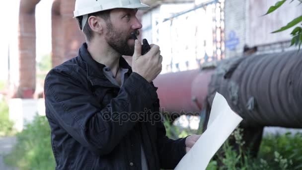 Ingenieur Mann Supervisor hält Baupläne und inspiziert die Pipeline. Inspektor spricht über Walkie-Talkie — Stockvideo