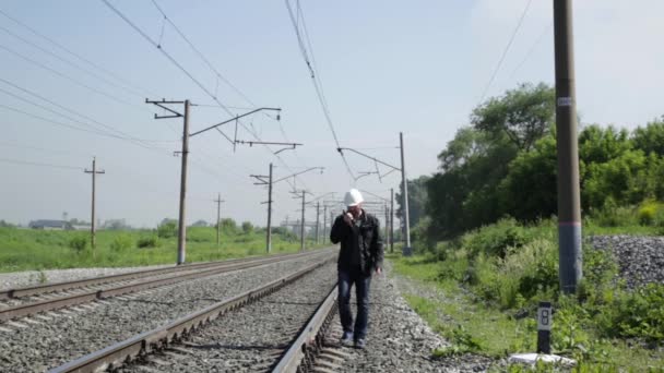 Inspecteur van het spoorwegverkeer geïrriteerd praten over walkie-talkie. Spoorweg werknemer in wit helm wandelen langs de spoorweg — Stockvideo