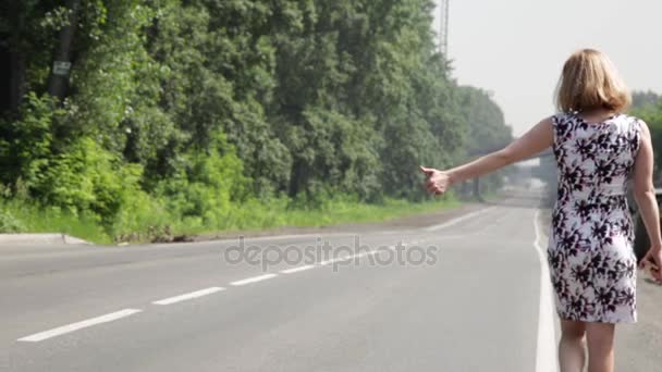Bela mulher pegar carro em uma estrada. menina andando ao longo da estrada — Vídeo de Stock
