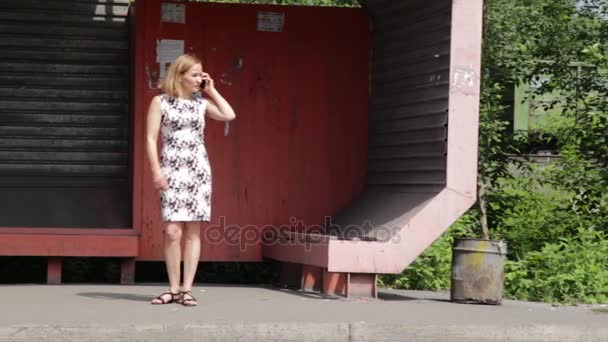 Молодая женщина использует мобильный телефон во время ожидания транспорта на автобусной остановке — стоковое видео