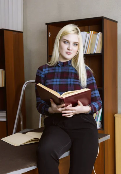 Jong meisje student permanent en het lezen boek in de buurt van boekenkasten in bibliotheek achtergrond — Stockfoto